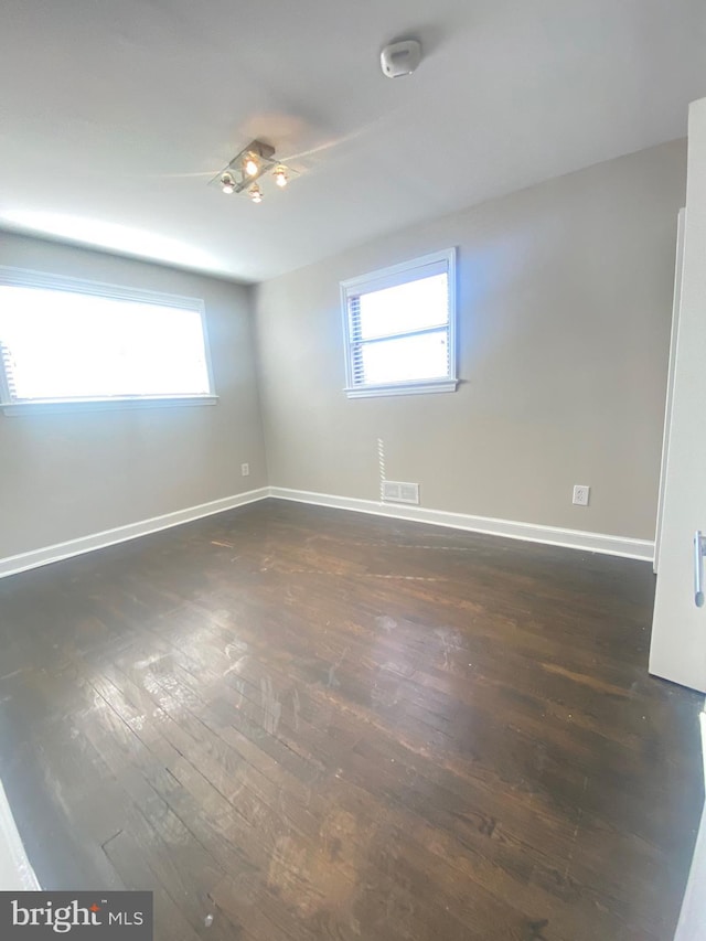 unfurnished room featuring dark wood finished floors, visible vents, and baseboards