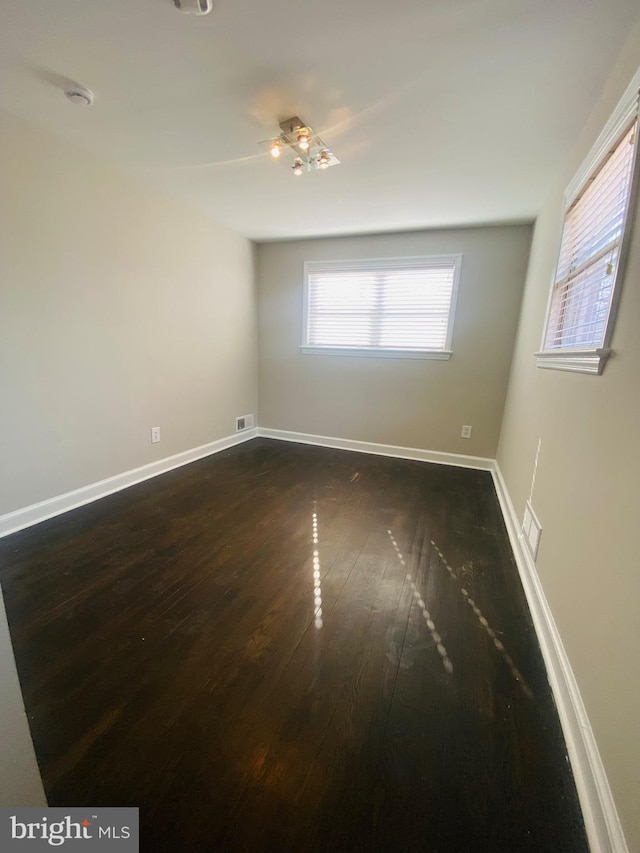 unfurnished room with dark wood-type flooring, visible vents, and baseboards