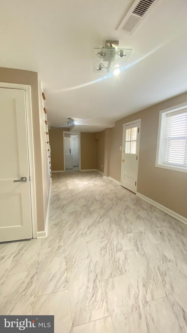 spare room with marble finish floor, plenty of natural light, visible vents, and baseboards