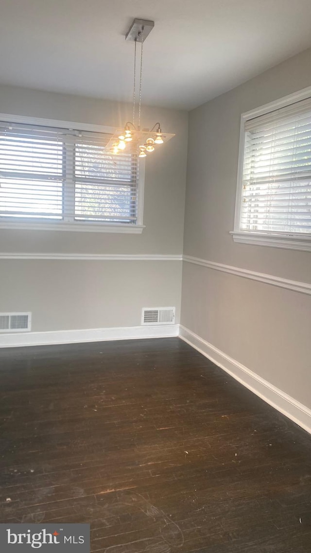 empty room with a chandelier, visible vents, and wood finished floors