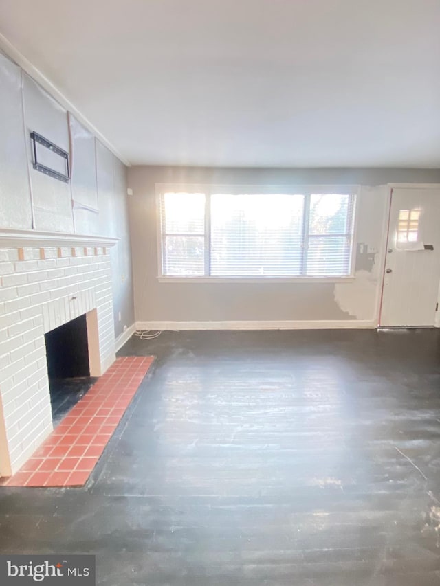 unfurnished living room with a brick fireplace, baseboards, and wood finished floors