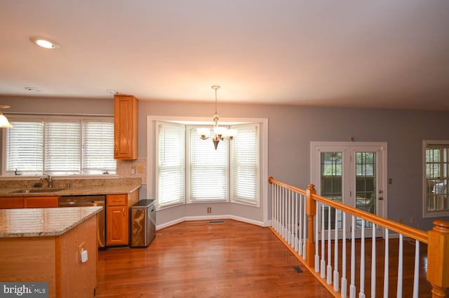 kitchen with sink, stainless steel dishwasher, light stone countertops, wood-type flooring, and a notable chandelier