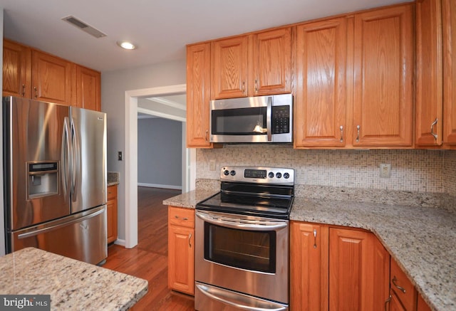 kitchen with light stone countertops, light hardwood / wood-style flooring, stainless steel appliances, and tasteful backsplash