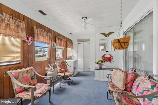 living area with wooden walls, ceiling fan, and carpet