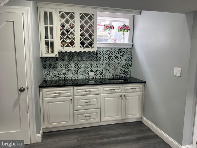 bar featuring backsplash, sink, white cabinets, and dark wood-type flooring