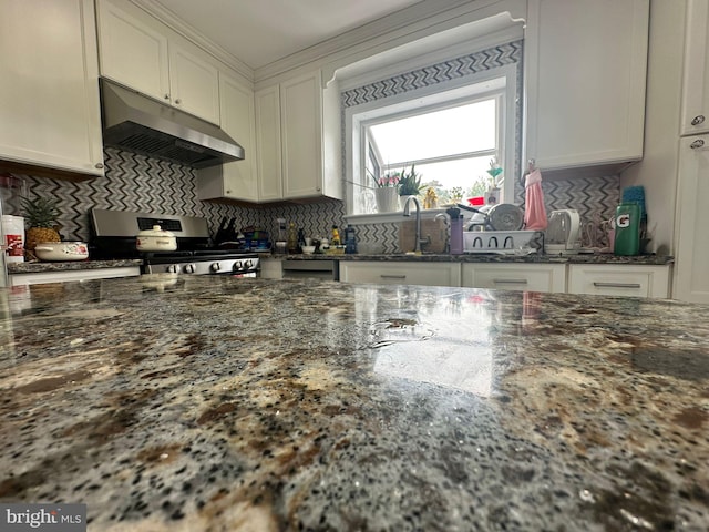 kitchen featuring dark stone counters, sink, stainless steel gas range, decorative backsplash, and white cabinetry