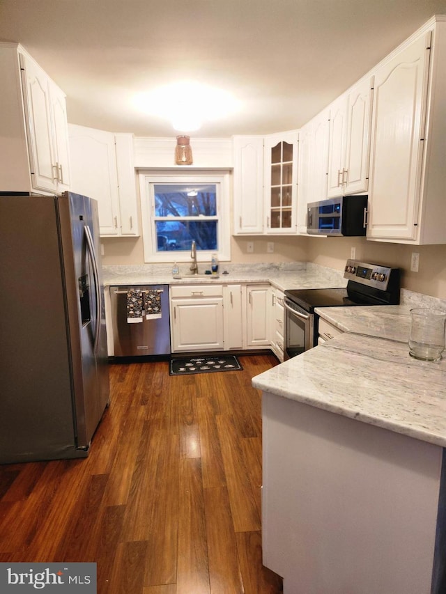 kitchen featuring appliances with stainless steel finishes, glass insert cabinets, white cabinetry, a sink, and light stone countertops