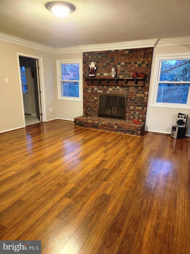 unfurnished living room with a textured ceiling, a brick fireplace, wood finished floors, and crown molding