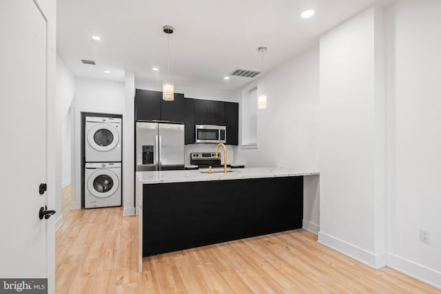 kitchen with stainless steel appliances, stacked washer / drying machine, kitchen peninsula, and sink