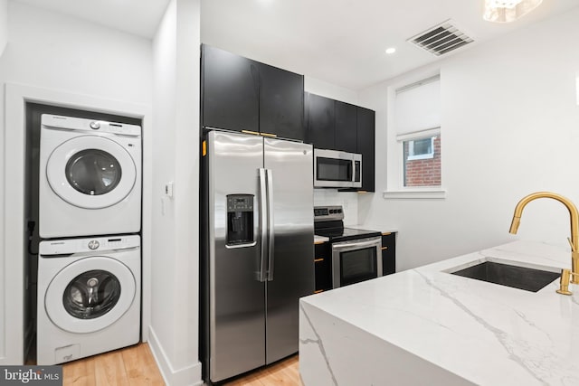 kitchen featuring sink, light wood-type flooring, stacked washer and dryer, appliances with stainless steel finishes, and light stone counters