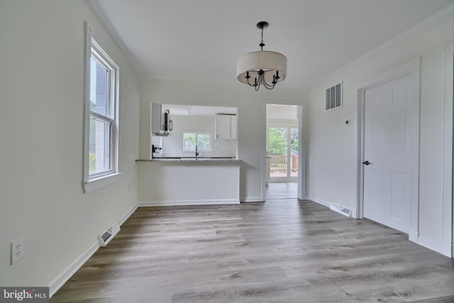 unfurnished living room featuring ornamental molding, a notable chandelier, and light hardwood / wood-style floors