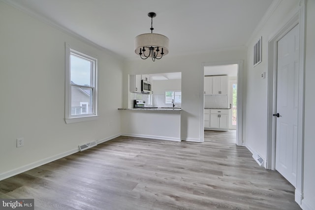 unfurnished dining area with ornamental molding, sink, an inviting chandelier, and light wood-type flooring