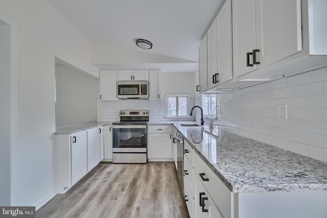 kitchen with lofted ceiling, sink, appliances with stainless steel finishes, light hardwood / wood-style floors, and white cabinets