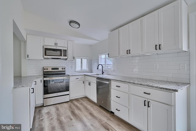 kitchen featuring stainless steel appliances, white cabinets, light stone counters, and light hardwood / wood-style floors