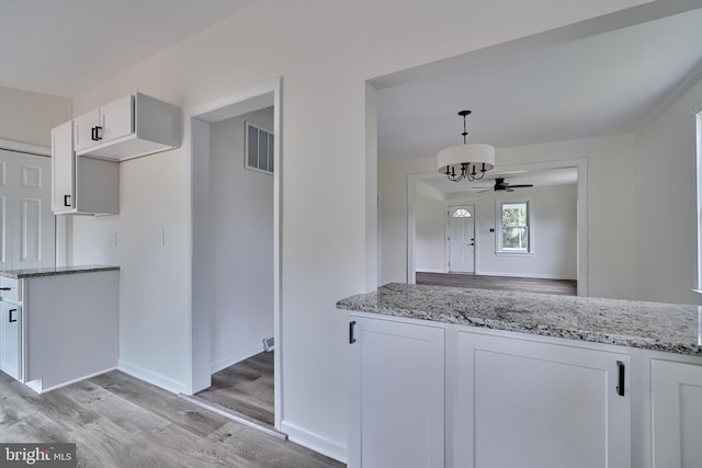 kitchen with pendant lighting, white cabinets, light stone counters, and light hardwood / wood-style flooring