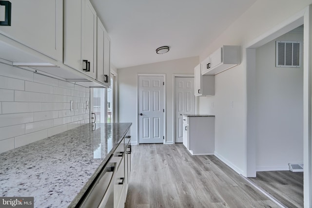 kitchen featuring white cabinetry, lofted ceiling, decorative backsplash, light stone counters, and light wood-type flooring