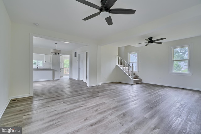 unfurnished living room featuring ceiling fan with notable chandelier and light hardwood / wood-style flooring