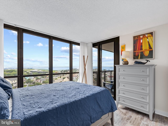 bedroom featuring a wall of windows, a textured ceiling, and light hardwood / wood-style floors