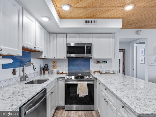 kitchen with appliances with stainless steel finishes, white cabinets, light hardwood / wood-style flooring, light stone counters, and sink