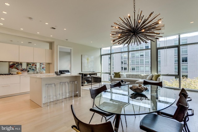 dining space featuring light wood-type flooring, a notable chandelier, sink, and floor to ceiling windows