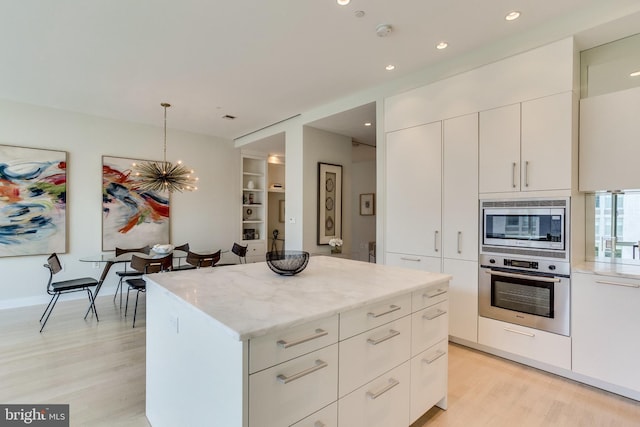 kitchen with appliances with stainless steel finishes, white cabinets, a kitchen island, and decorative light fixtures