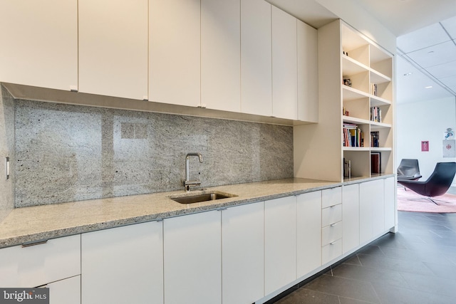 kitchen featuring decorative backsplash, light stone countertops, white cabinetry, and sink