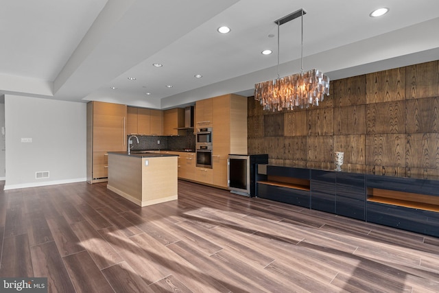 kitchen with sink, wall chimney range hood, tasteful backsplash, an island with sink, and decorative light fixtures