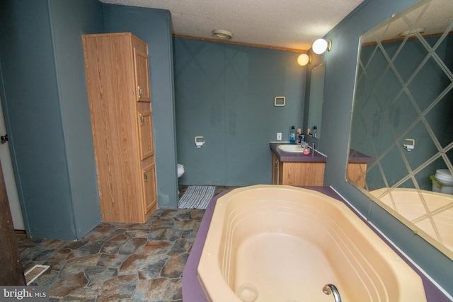 bathroom featuring a textured ceiling, vanity, toilet, and a tub to relax in