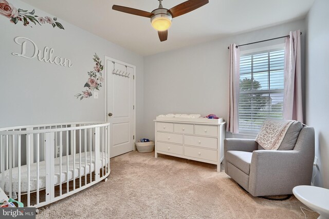 bedroom with ceiling fan, a nursery area, and light carpet