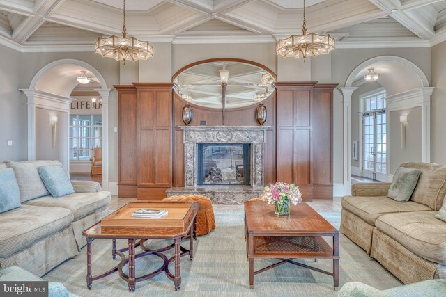 living room featuring a notable chandelier, coffered ceiling, crown molding, and ornate columns