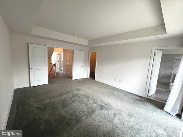 unfurnished bedroom featuring dark carpet, a tray ceiling, and ensuite bath