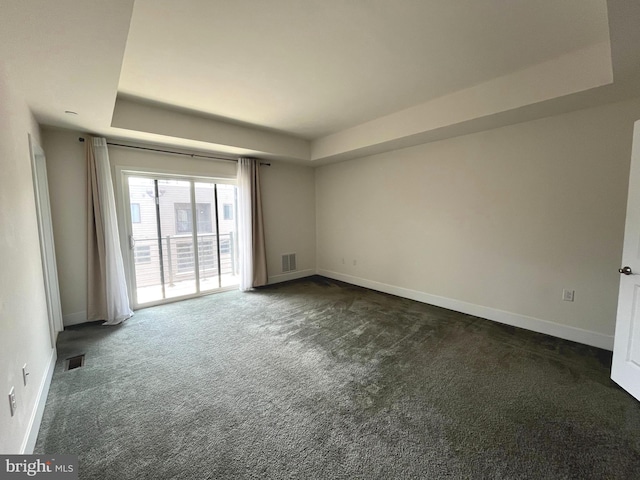 spare room featuring dark colored carpet and a raised ceiling