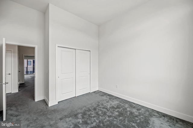 unfurnished bedroom featuring a closet, a towering ceiling, and dark carpet