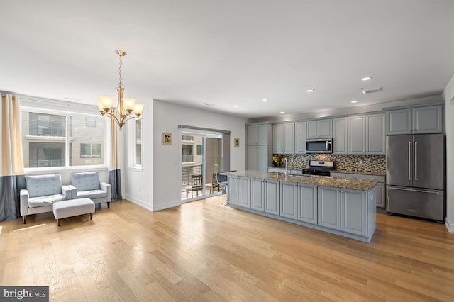 kitchen featuring a kitchen island with sink, light hardwood / wood-style flooring, hanging light fixtures, gray cabinetry, and stainless steel appliances