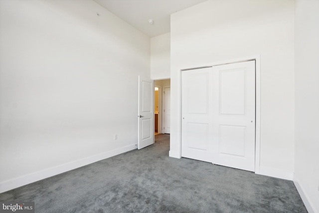 unfurnished bedroom featuring a high ceiling, dark colored carpet, and a closet