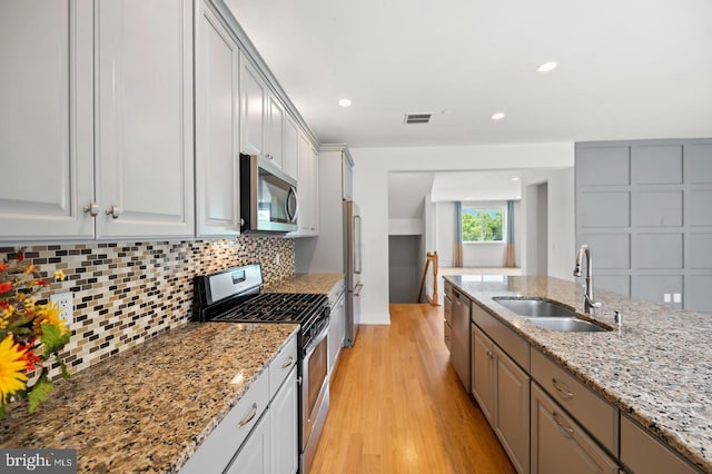 kitchen featuring tasteful backsplash, light stone countertops, sink, light wood-type flooring, and stainless steel appliances