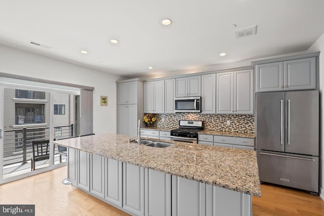 kitchen with gray cabinetry, stainless steel appliances, sink, and a kitchen island with sink