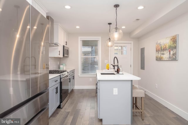 kitchen with white cabinets, backsplash, a kitchen island with sink, stainless steel appliances, and wood-type flooring