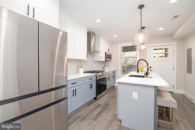 kitchen with stainless steel appliances, backsplash, a kitchen island with sink, light wood-type flooring, and wall chimney exhaust hood