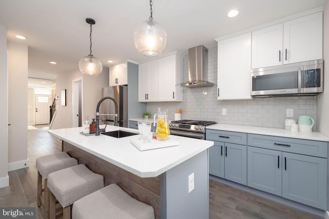 kitchen featuring decorative backsplash, stainless steel appliances, wood-type flooring, and wall chimney exhaust hood