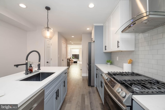 kitchen featuring backsplash, light hardwood / wood-style floors, appliances with stainless steel finishes, wall chimney exhaust hood, and sink