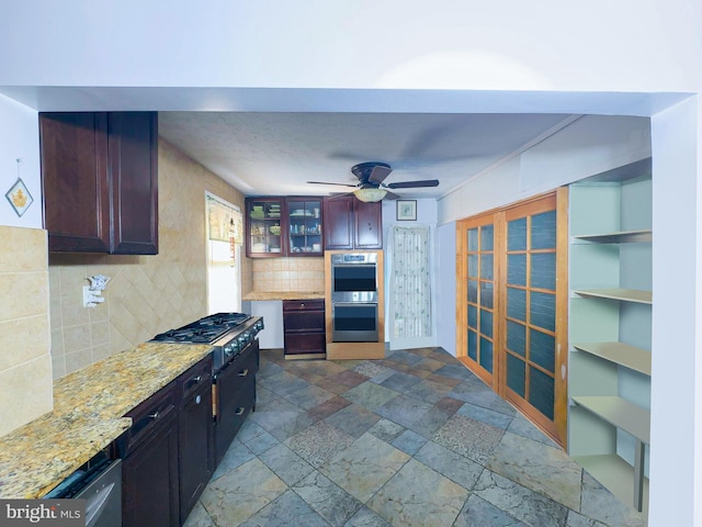 kitchen with stainless steel double oven, ceiling fan, tasteful backsplash, gas stovetop, and light stone counters