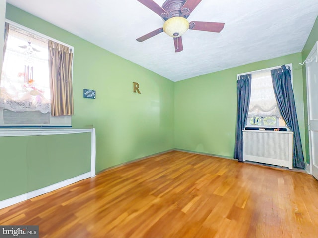 unfurnished room featuring ceiling fan, hardwood / wood-style floors, and radiator heating unit