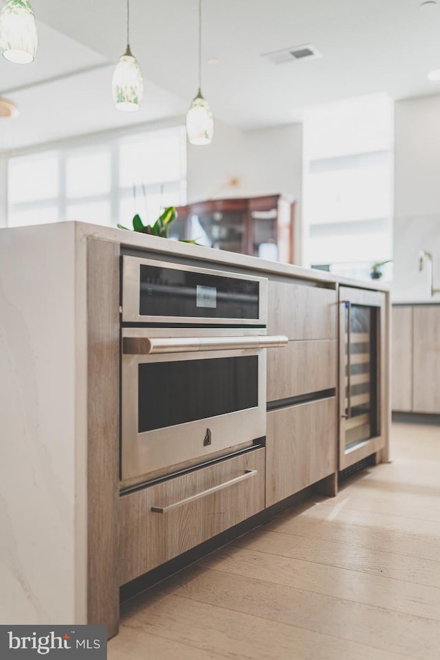 kitchen featuring wine cooler, light hardwood / wood-style flooring, oven, and decorative light fixtures