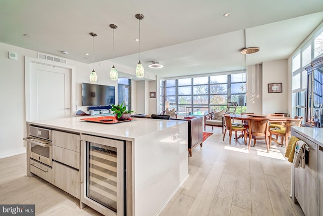 kitchen with light brown cabinetry, beverage cooler, pendant lighting, light hardwood / wood-style flooring, and a center island