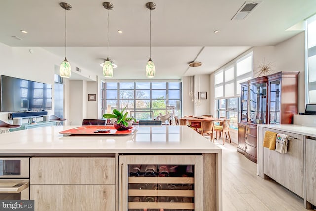 kitchen featuring light brown cabinets, beverage cooler, light hardwood / wood-style flooring, pendant lighting, and a kitchen island