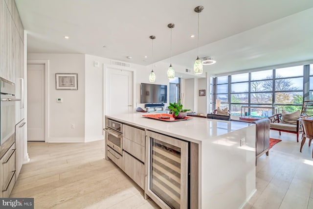 kitchen featuring light brown cabinetry, wine cooler, a center island, and pendant lighting