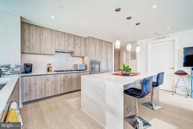 kitchen with a center island, white gas cooktop, oven, pendant lighting, and a breakfast bar