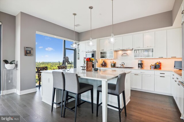 kitchen featuring white cabinets, dark hardwood / wood-style flooring, an island with sink, decorative backsplash, and a breakfast bar area