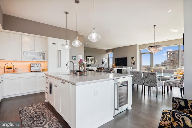 kitchen featuring wine cooler, decorative light fixtures, sink, an island with sink, and white cabinets